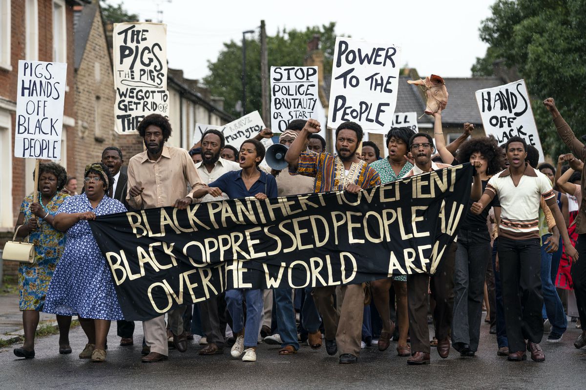 En stor grupp av svarta demonstranter bär en Black Panther-banner i Steve McQueens filmfilm Mangrove från Small Axe