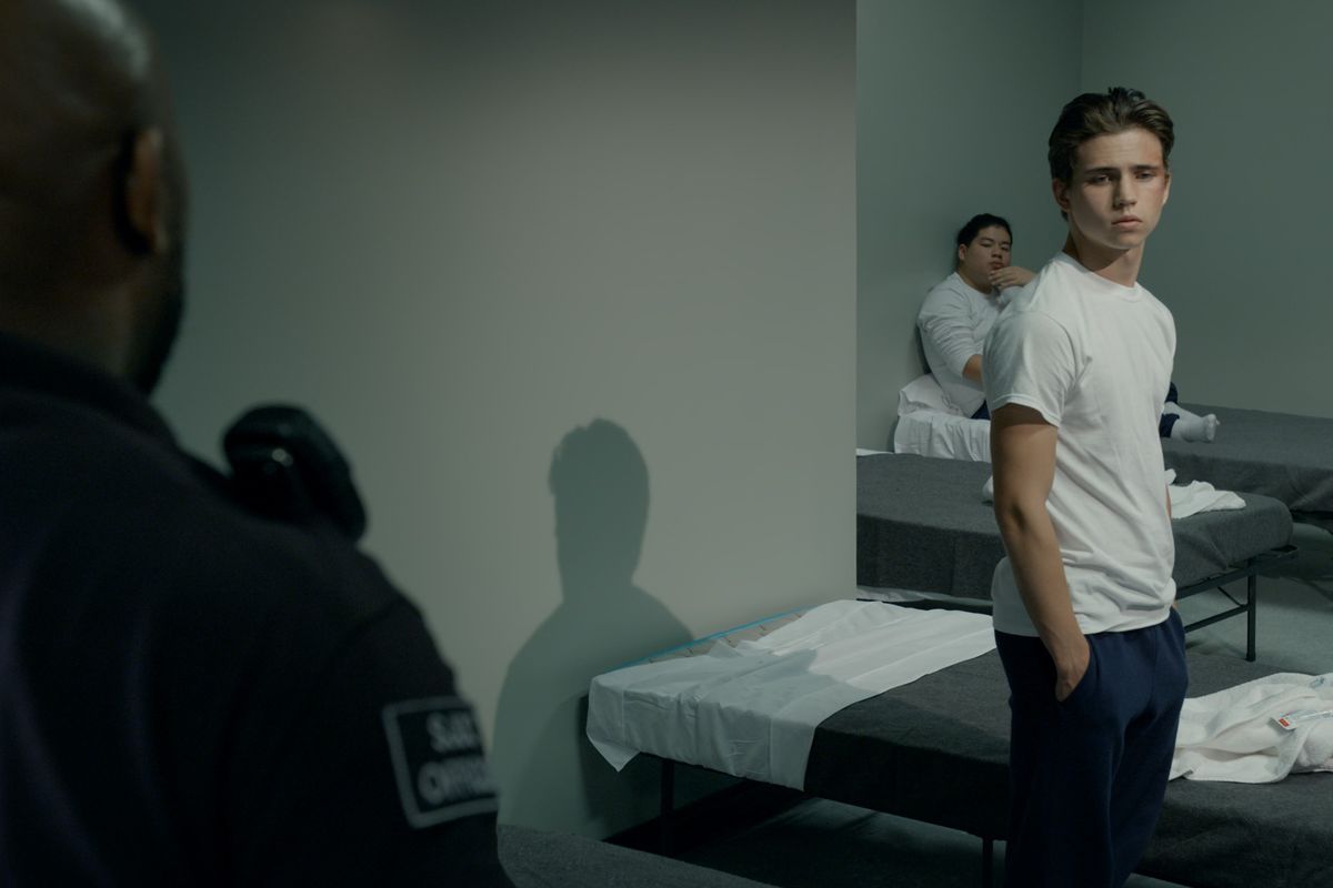 Robbie Keene (Tanner Buchanan) står vid sin fängelsesäng med händerna i fickorna och tittar bort från en vakt i förgrunden.