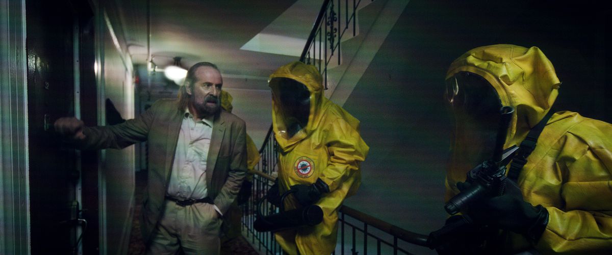 Peter Stormare pekar två personer i gula HAZMAT-dräkter på en lägenhetsdörr i Songbird