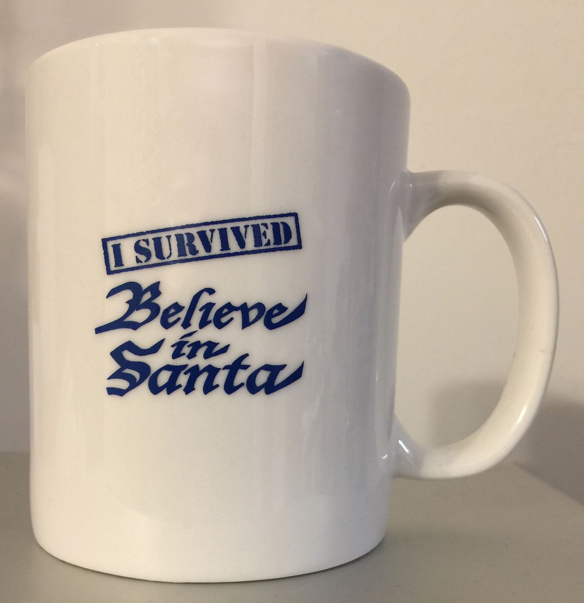 a cream-colored mug saying “I survived Believe in Santa”