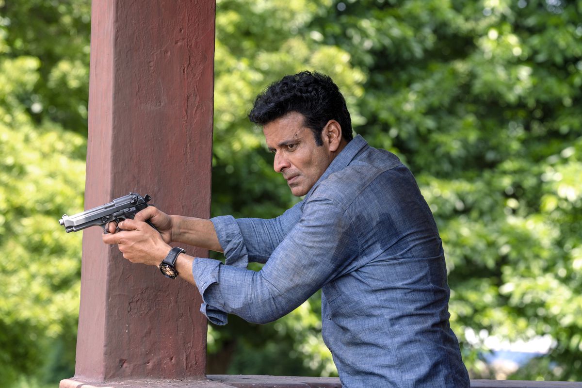 Manoj Bajpayee holds a gun while wearing a light blue shirt in The Family Man.