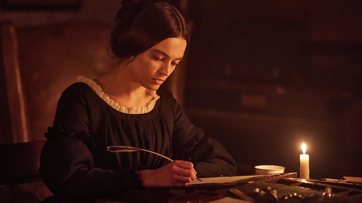 Emma Mackey som Emily Brontë skriver på en bit pergament med en fjäderpenna vid levande ljus i Emily.