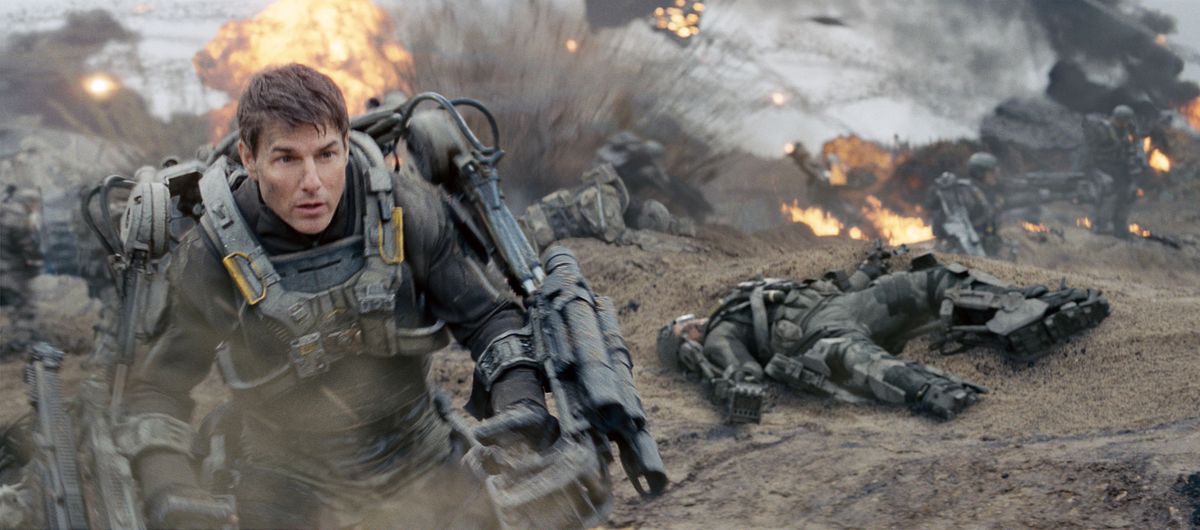 Tom Cruise som Cage i kraftrustning stormar en strand fylld av explosioner i Edge of Tomorrow.