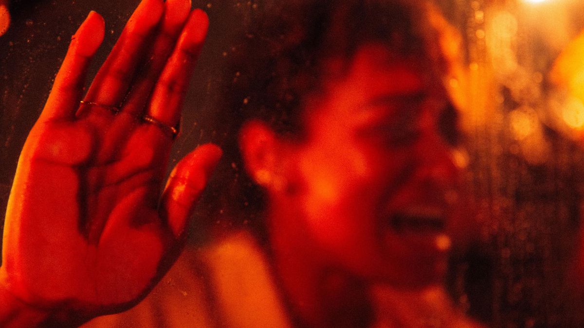 A close-up of a woman screaming in a car in Talk to Me. The image is tinted in red, and her hand is pressed up against the glass window.