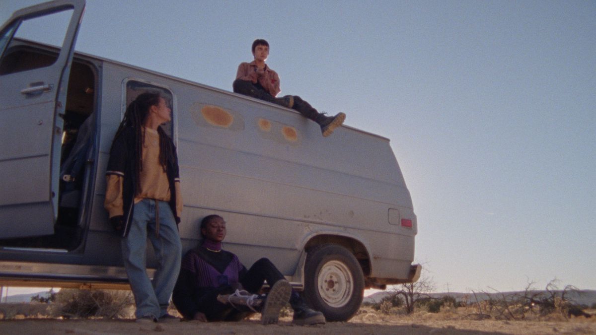 The young people in How to Blow Up a Pipeline sit on top of and in front of a white van. One leans against it. The background is the desolate West Texas desert.