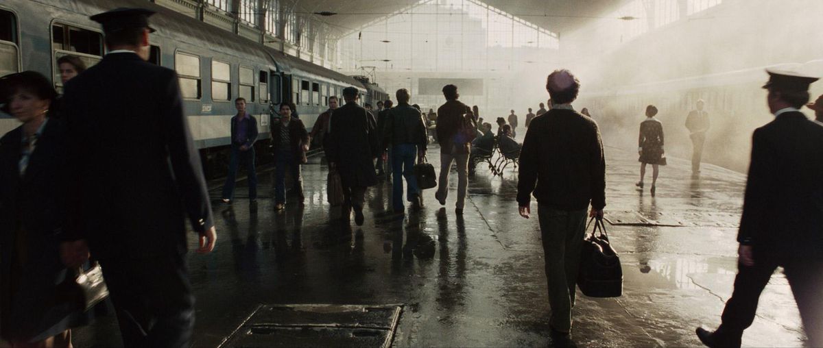 Passagerare som bär resväskor går bredvid ett tåg på en station upplyst med ljusa utblåsta fönsterljus, och kastar varje person i siluett i München 