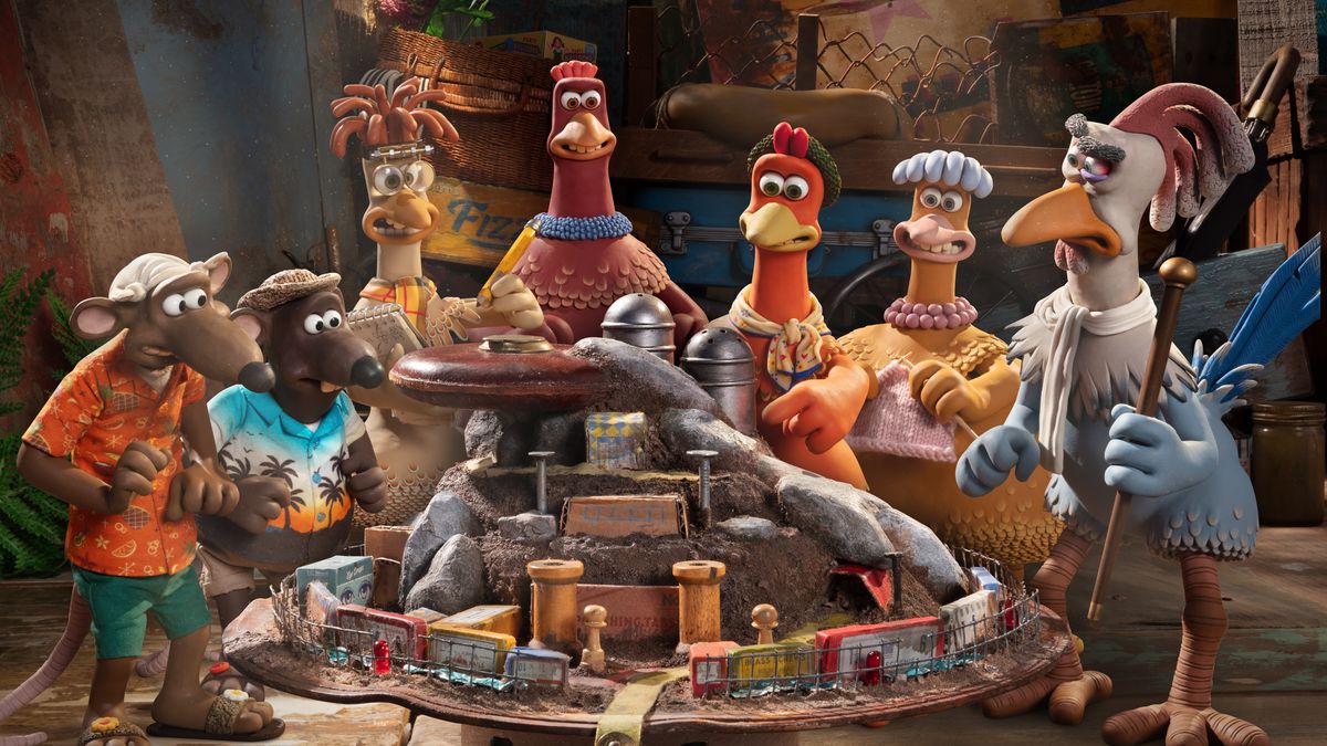 Characters from 2000’s Claymation feature Chicken Run stand in a semicircle in the sequel, Chicken Run: Dawn of the Nugget, surrounding a large model seemingly depicting a domed city covered with rocks and surrounded by fencing and electronics. Pictured: Rats Fetcher and Nick, chickens Mac, Bunty, Ginger, and Babs, and grey-feathered rooster Fowler.
