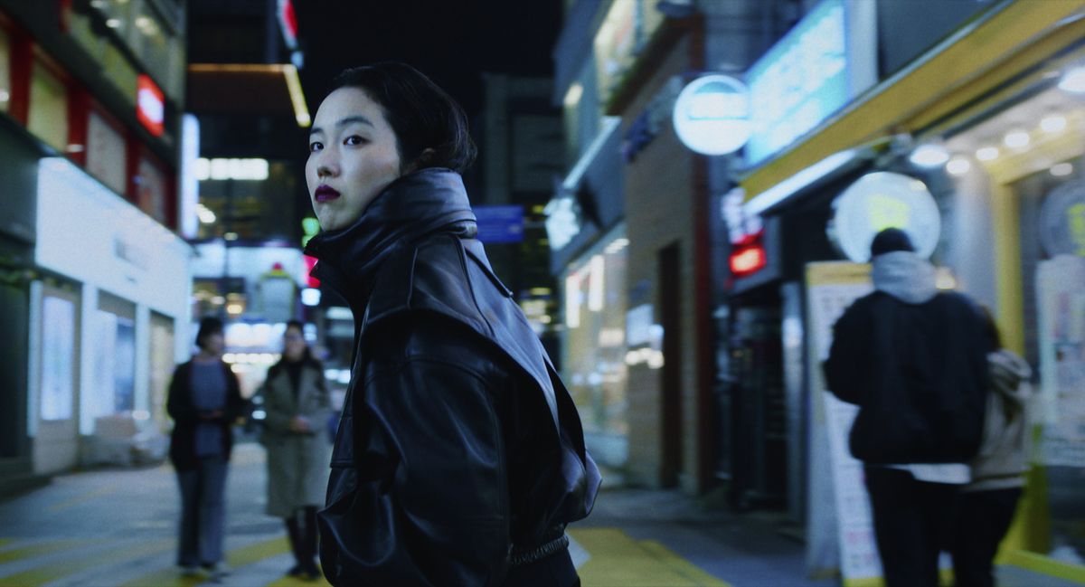 Jin-Min Park som Freddie, klädd i mörkrött läppstift i en svart läderrock stående mitt på en koreansk stadsgata på natten i Return to Seoul.