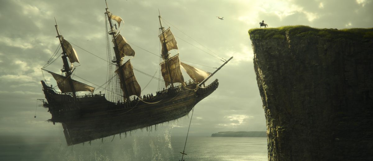Ett flygande skepp med segel svävar över vattnet och närmar sig en klippsida, där en figur sitter på en häst i Peter Pan och Wendy.