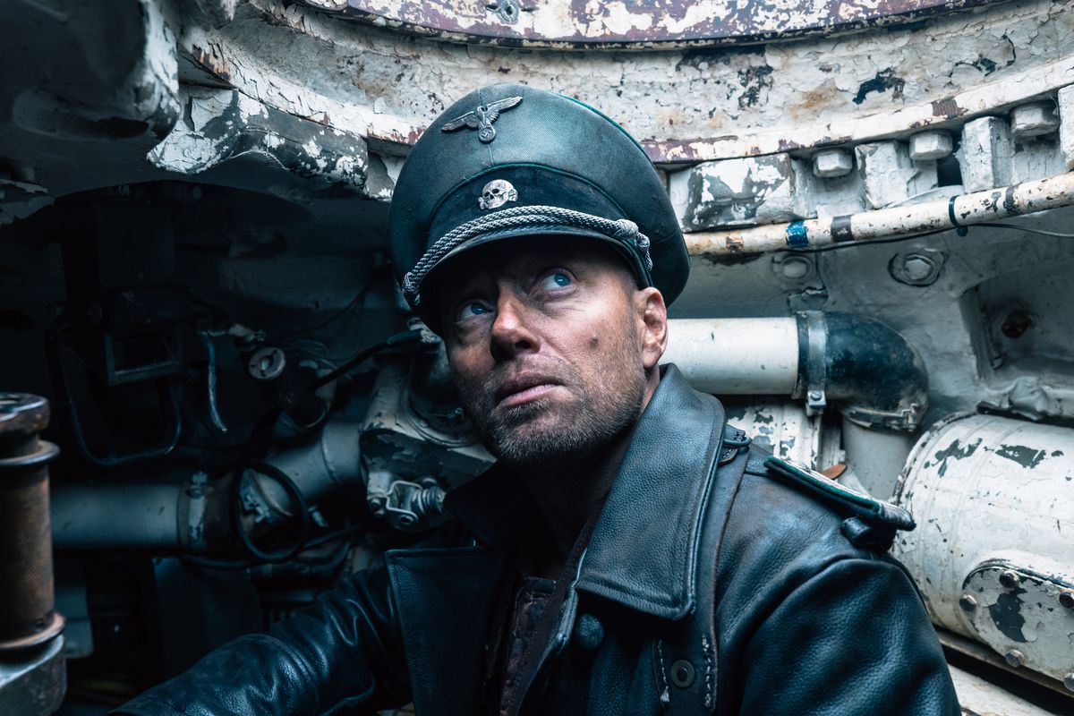 Aksel Hennie sitter i en stridsvagn iklädd sin nazistregalier i Sisu.  Han tittar uppåt mot himlen.