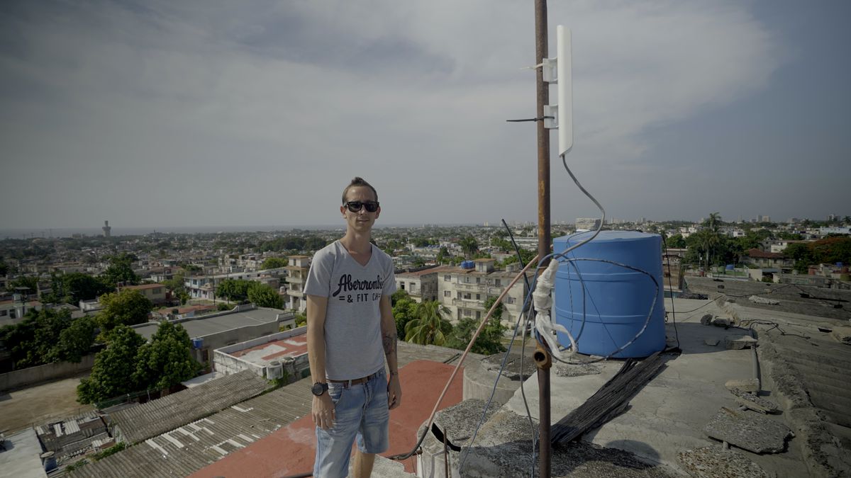 En kubansk tonåring i solglasögon i en Abercrombie-t-shirt och jeansshorts står vid en mottagarstång för SNET-signalen