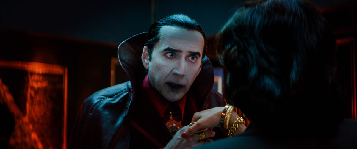 Nicolas Cage som en mycket traditionell film Count Dracula (blek-som-papper-hud, slicked-back-svart hår med en änkans topp, svart cape med en enorm hög krage, hungrig blick i hans ögon) tar handen av en kvinna med ryggen till kameran i Renfield