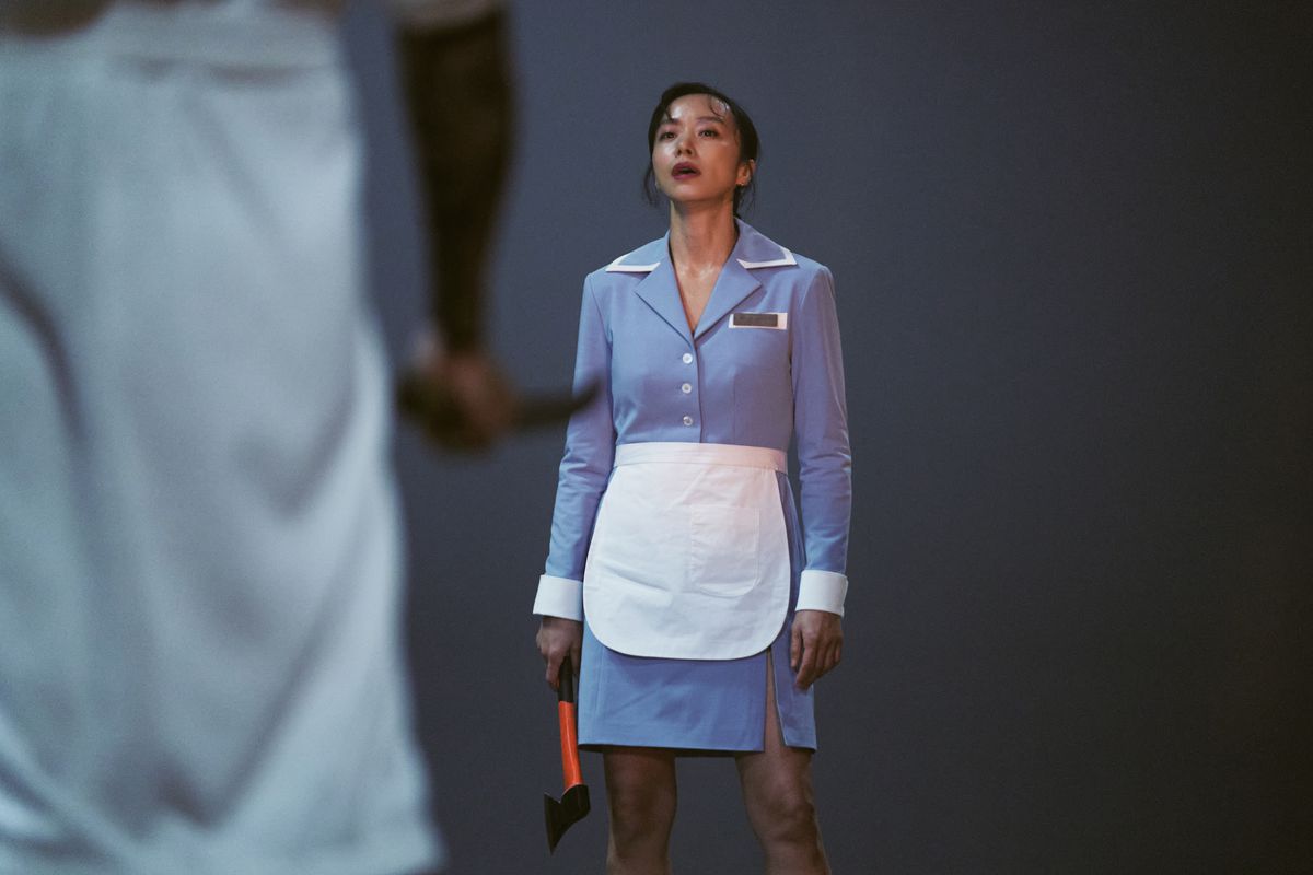 Jeon Do-yeon as Boksoon looks tired while wearing a uniform with an apron and holding a hatchet in Kill Boksoon.