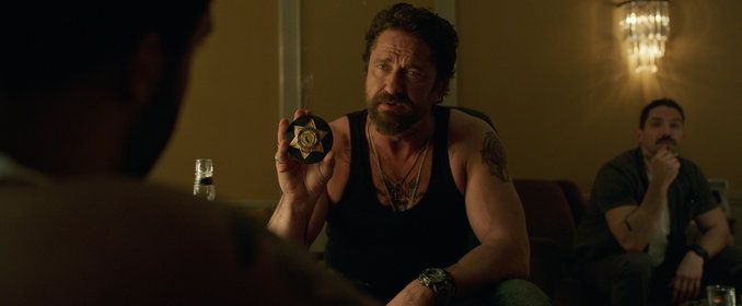 Gerard Butler wears a black tanktop and flashes his LAPD badge at O’Shea Jackson Jr. in Den of Thieves.