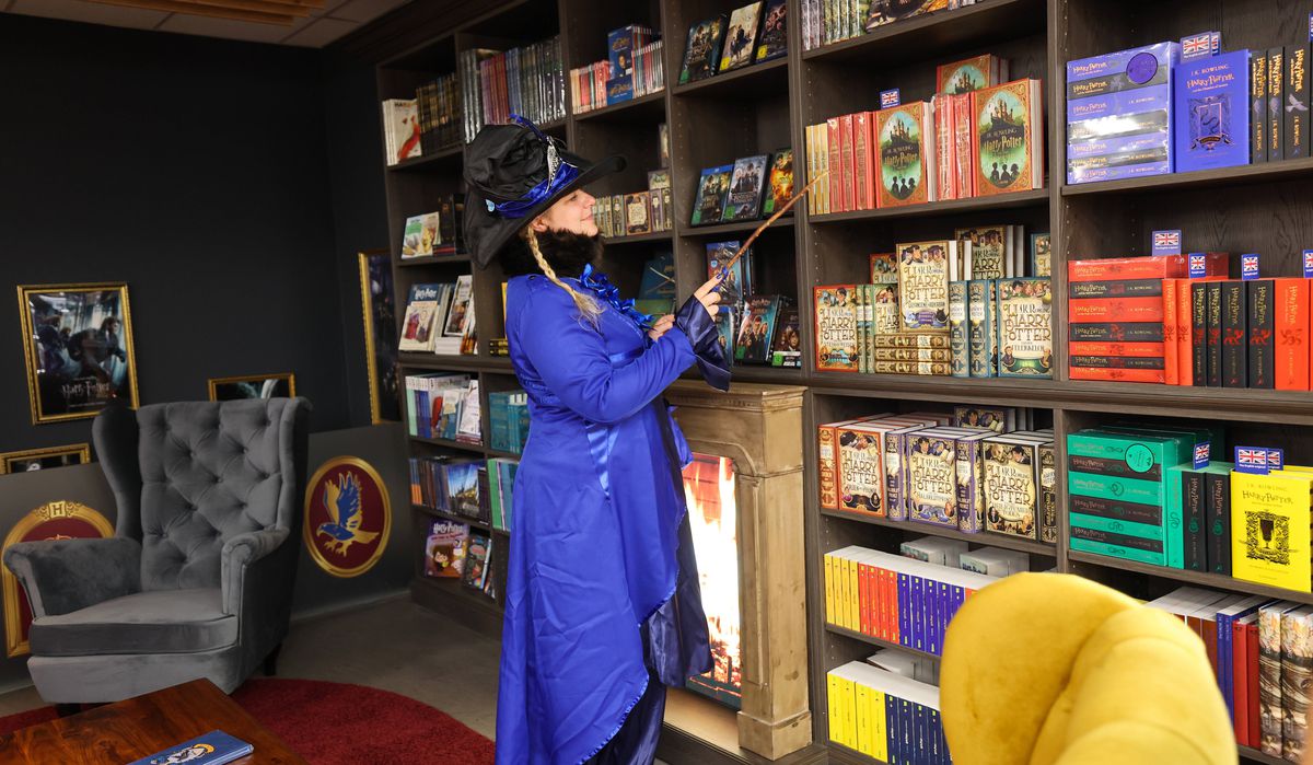 En besökare i en lila dräkt, som håller i en trollstav, tittar på en vägg av Harry Potter-böcker och varor vid invigningen av The Wizard World Shop – av Thalia i Hamburg.