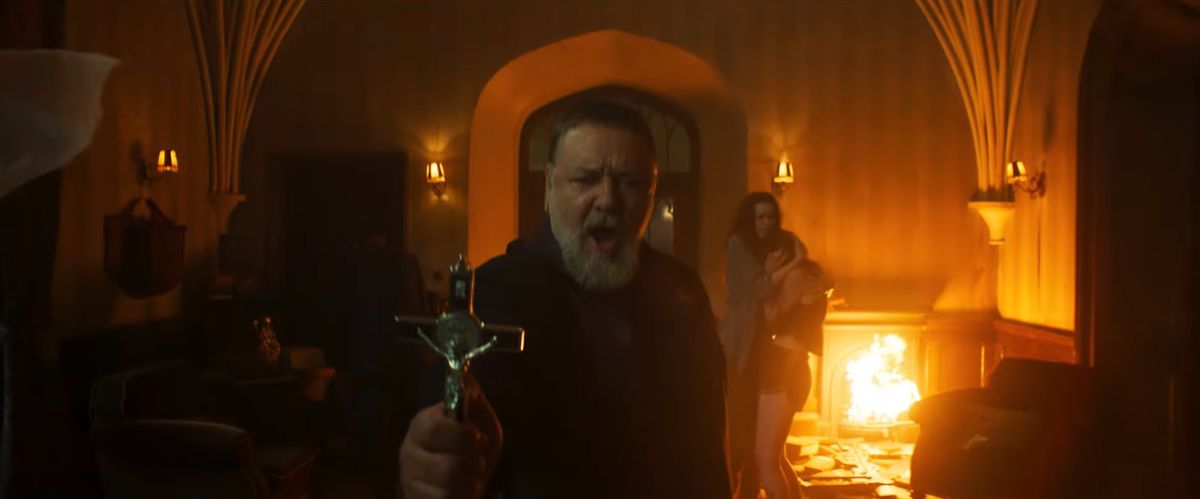 Russell Crowe håller upp ett kors med lågor bakom sig i The Pope's Exorcist.