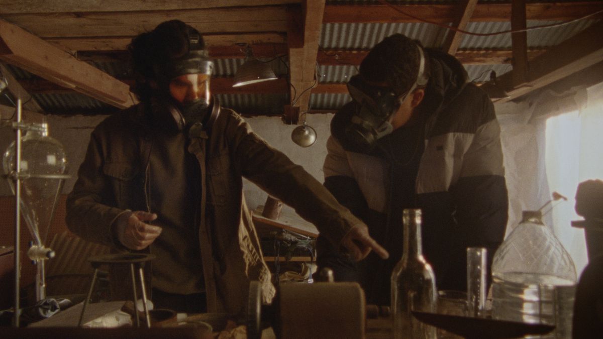Två personer som bär gasmasker arbetar med kemikalier, medan en pekar, i How to Blow Up a Pipeline.