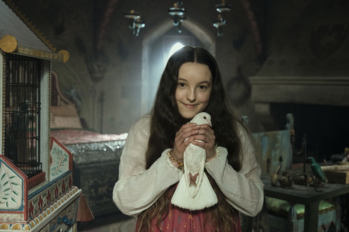 A girl in a dark bedroom clutches a bird in her hands and smiles at the camera.