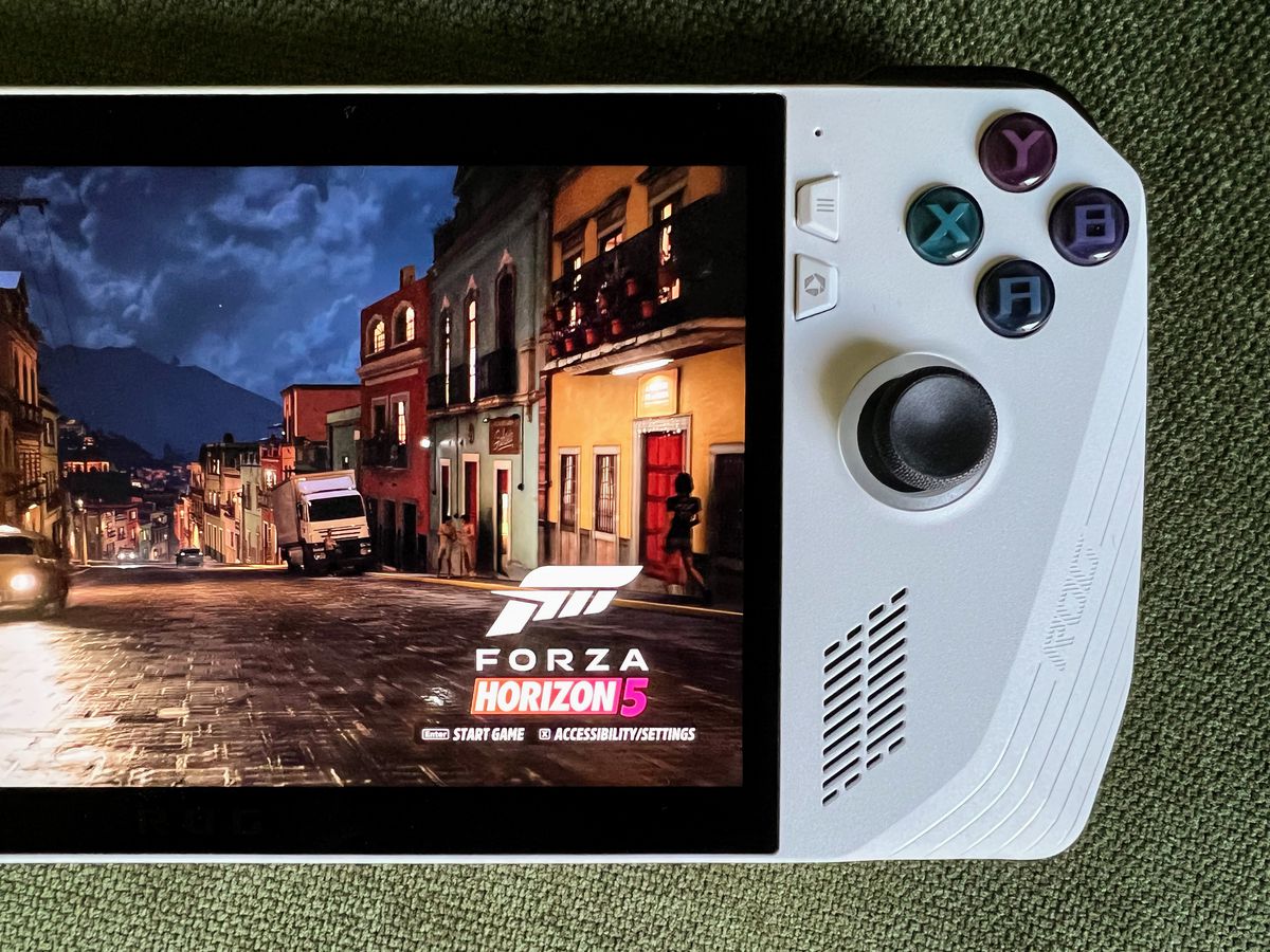 en regnig gatuscen i Forza Horizon 5 som körs på en Asus ROG Ally gaming-handdator, liggande på olivgrönt tyg, i ett närbild över huvudet av enhetens högra sida