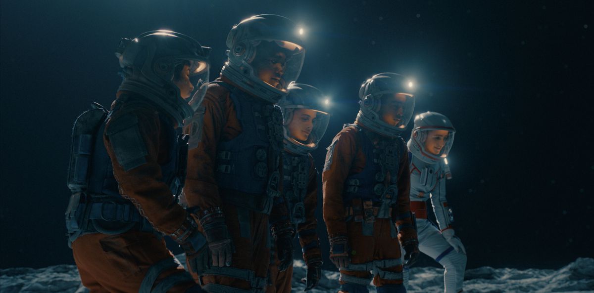 Fem tonåringar i rymddräkter som går över månens yta. 