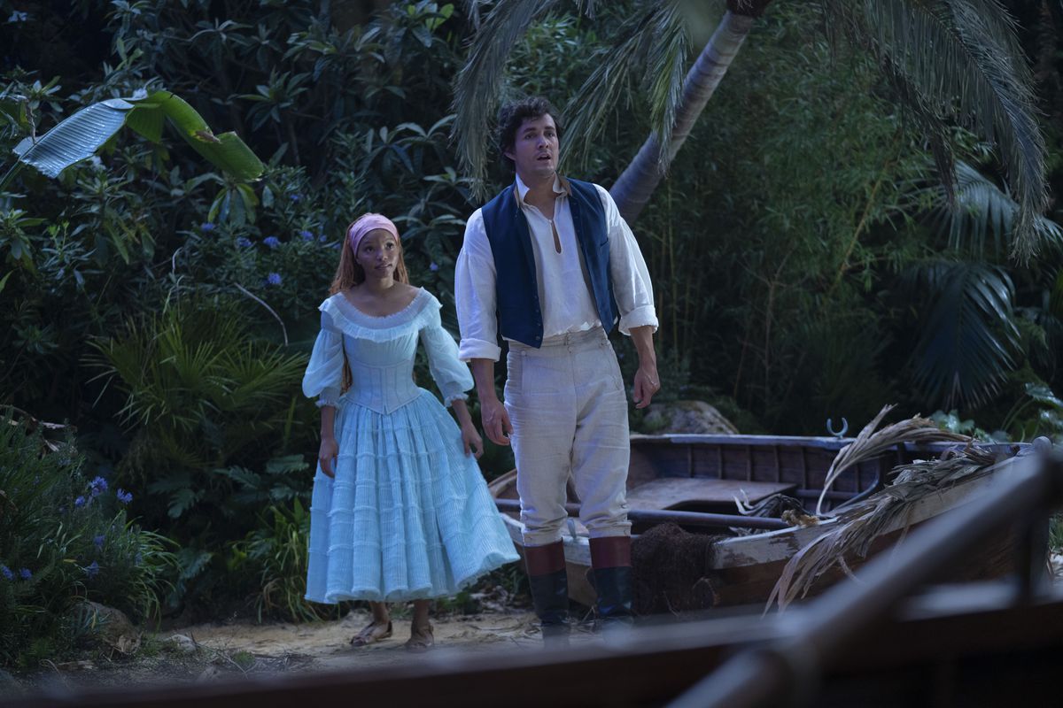 Eric och Ariel i live-action Little Mermaid står på en strand.  Ariel bär en ljusblå klänning, medan Eric bär en vit skjorta med blå väst och khakibyxor.
