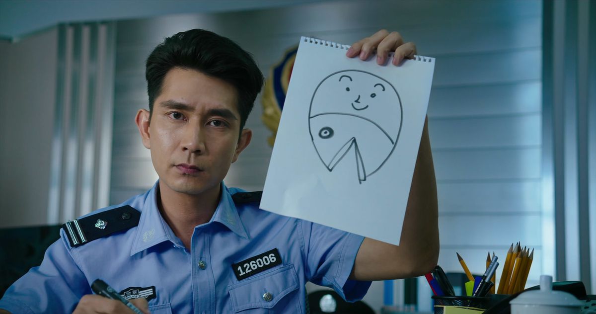 Sheung-ching Lee, wearing a blue police uniform, holds a hilarious drawing of a “half-person, half-fish” mermaid, which is just a human face on top of a fish face. He has a straight face while doing this.