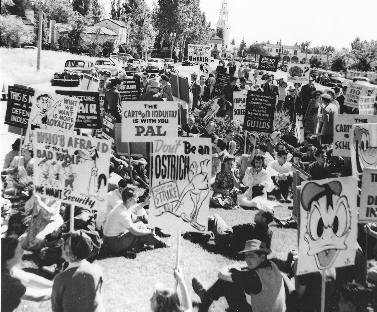 Archival image of strikers during the Disney Animators Strike, holding hand painted picket signs depicting well-known Disney characters like Daffy Duck and the Three Little Pigs. 