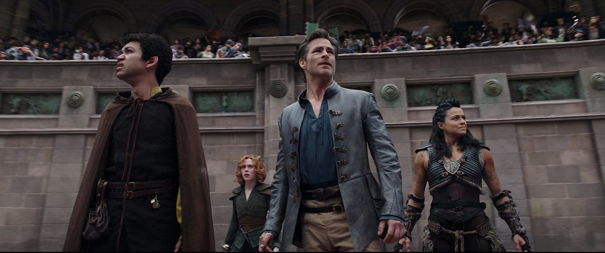 The four party members in Dungeons & Dragons: Honor Among Thieves — Simon (Justice Smith), Doric (Sophia Lillis), Edgin (Chris Pine) and Holga (Michelle Rodriguez) stand in front of a crowd in a gladiatorial arena, and look collectively worried