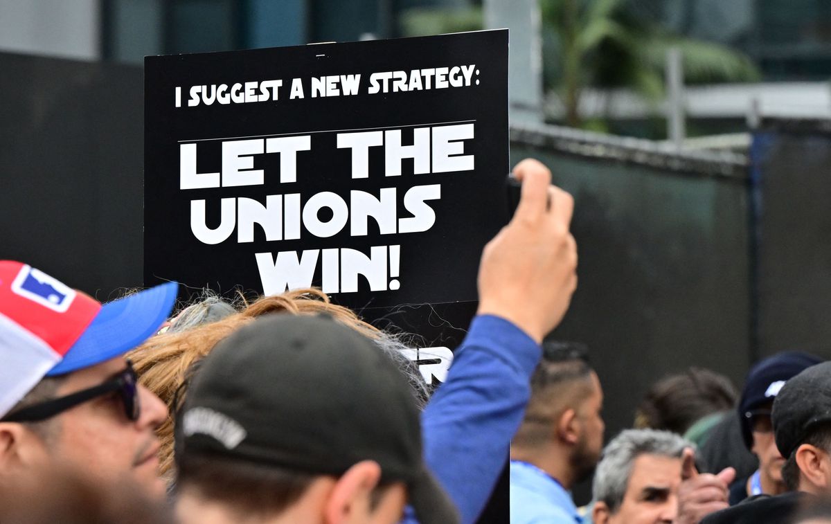 Demonstranter håller skyltar medan de strejkar under den fortsatta strejken av Writers Guild of America (WGA) i Los Angeles, Kalifornien, den 26 maj 2023. I mitten av bilden finns en skylt i Star Wars-titelfonten som säger 
