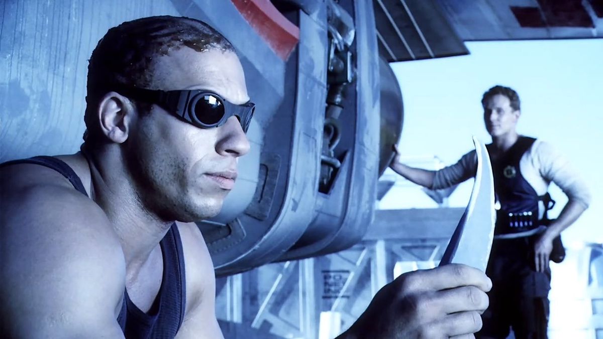 (LR) Richard B. Riddick (Vin Diesel) stirrar på en kniv med William J. Johns (Cole Hauser) i bakgrunden i Pitch Black.