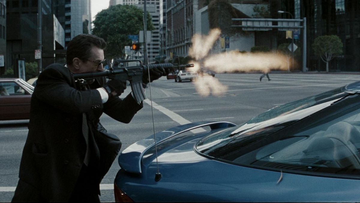Neil McCauley (Robert De Niro) avlossar ett M4A4-gevär bakom en blå bil i en korsning i Los Angeles, en mynningsblixt som syns utbrott från gevärets pipa i Heat.