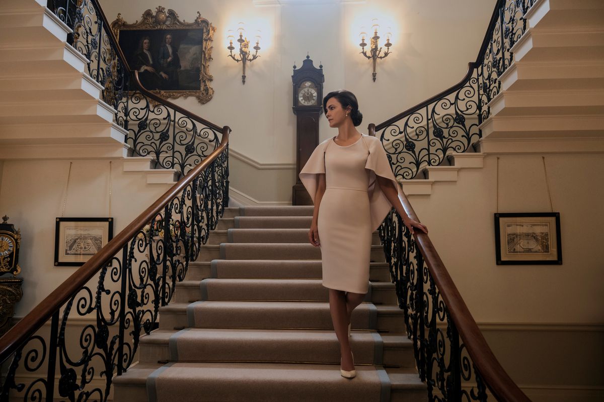 Keri Russell går nerför en extravagant trappa iförd en snygg beige-aktig klänning i The Diplomat.