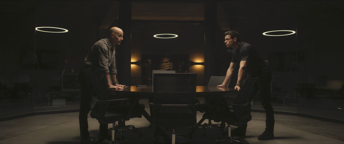 Bernard (Stanley Tucci) och Mason (Richard Madden) lutar sig över motsatta ändar av ett bord och tittar på varandra i en stillbild från Citadel säsong 1