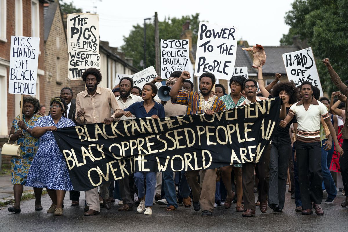 A large group of Black protestors carry a Black Panther banner in Steve McQueen’s Small Axe series movie Mangrove