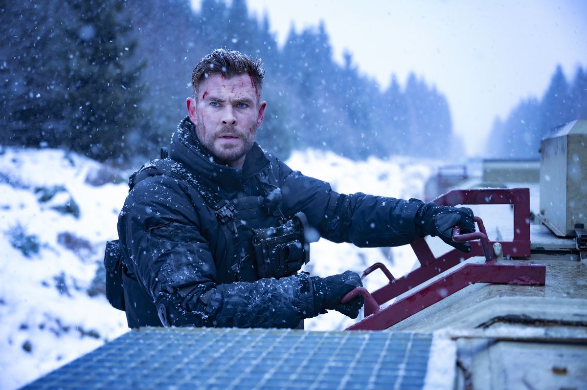 Chris Hemsworth sits on a snowmobile in the snow facing the camera with a tactical vest on in Netflix’s Extraction 2