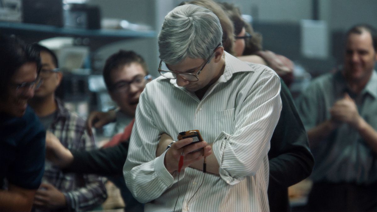 Jay Baruchel som en man med grått hår och glasögon (Mike Lazaridis) som håller i en prototyp av BlackBerry-enhet i BlackBerry.