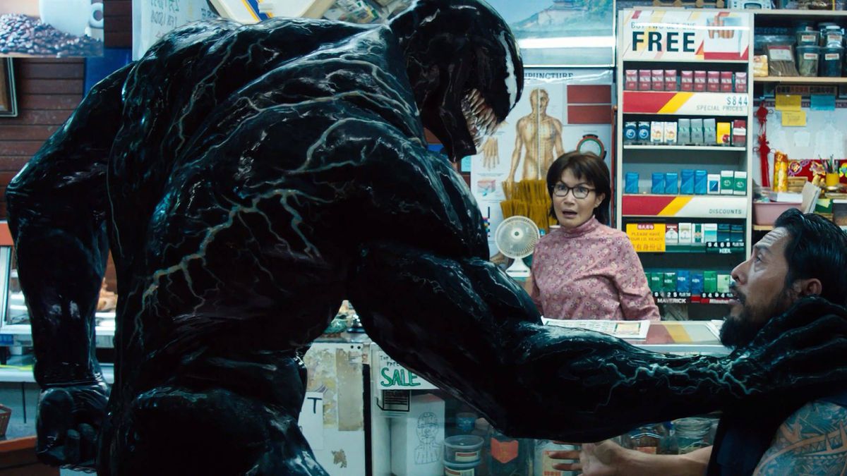 (LR) Venom (Tom Hardy) hotar en inbrottstjuv framför Mrs Chen (Peggy Lu) i Venom.