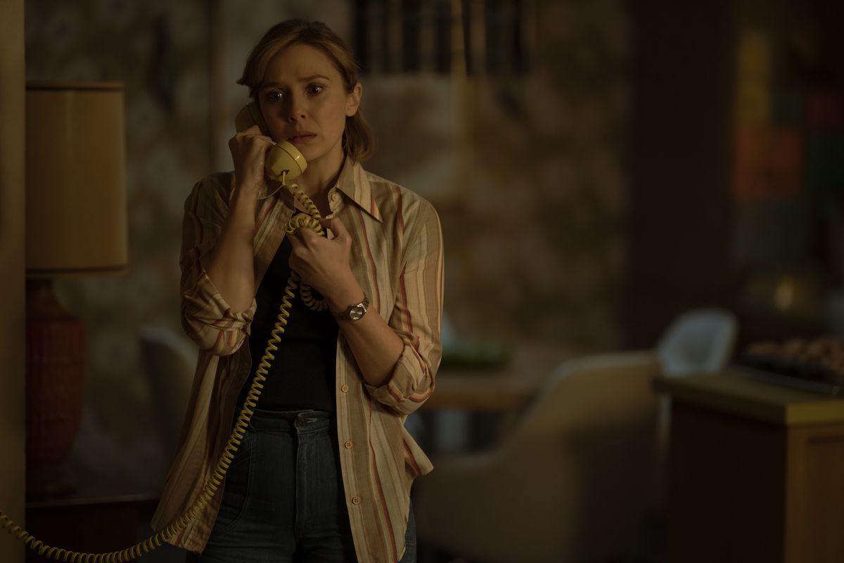 Candy (Elizabeth Olsen) stands and looks concerned on the phone 