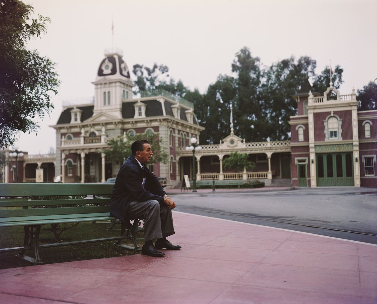 Walt Disney in an undated promotional portrait from the 1950s, sitting pensively alone on a bench at an empty Disneyland