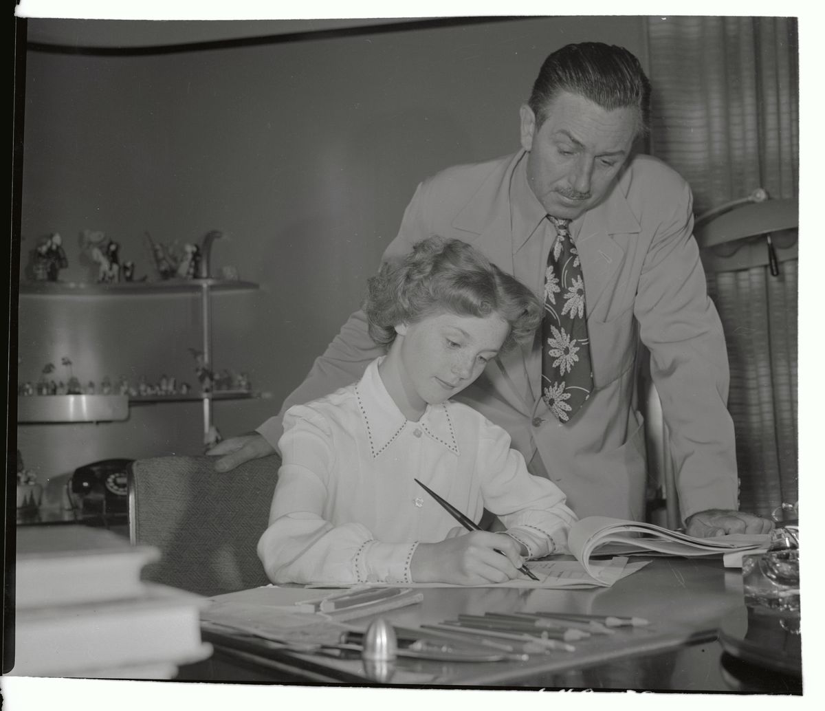 In an undated archival photo, Walt Disney leans over a desk where actor Kathryn Beaumont, the voice and live-action reference for Alice in Disney’s Alice in Wonderland and for Wendy Darling in Disney’s Peter Pan, signs a contract