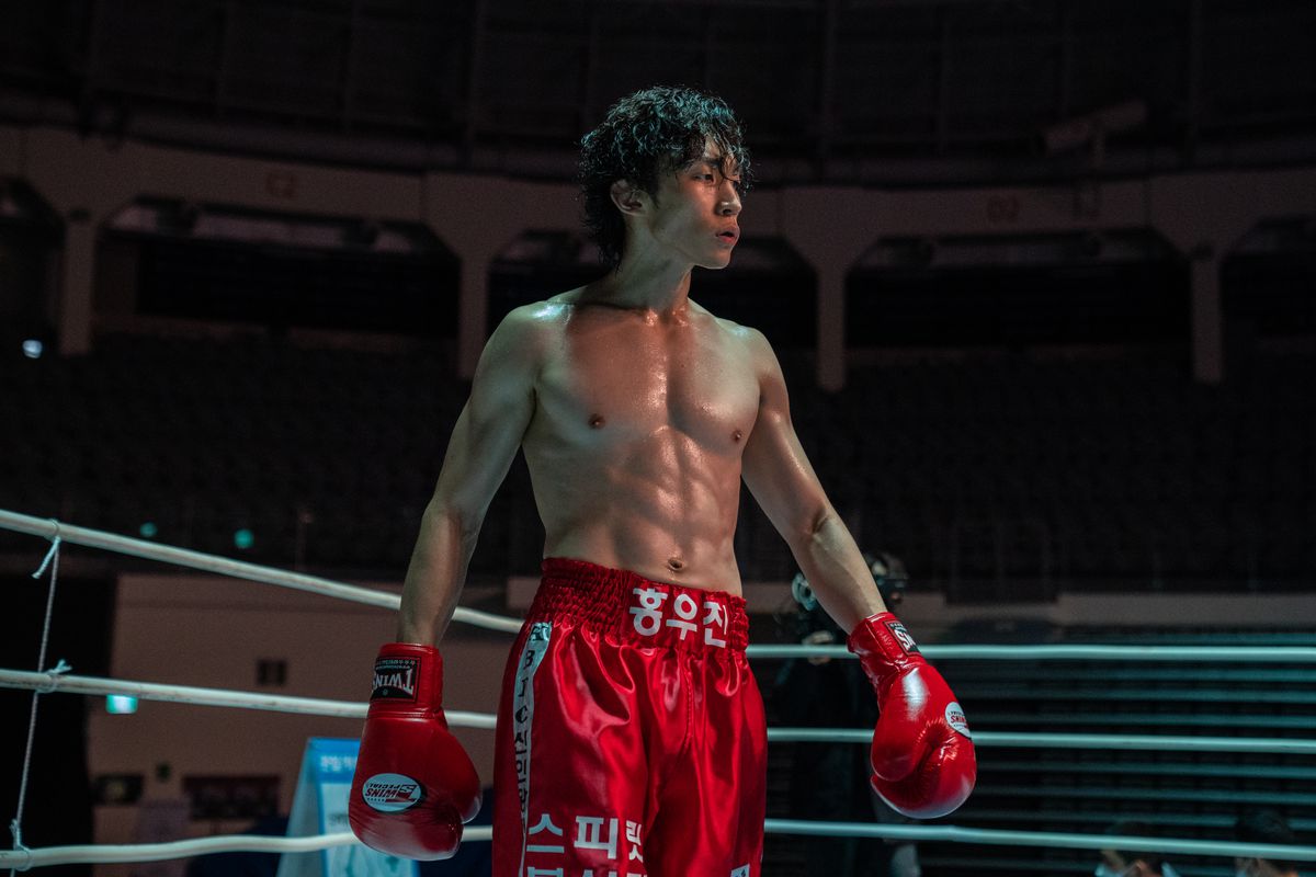 Hong Woo-jin strutsar i boxningsringen med röda trunkar och röda handskar i Bloodhounds.