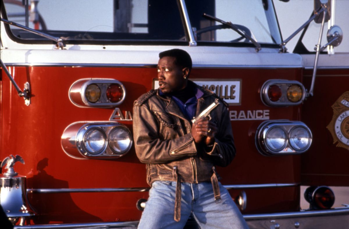 Wesley Snipes holds a gun and takes cover in front of an ambulance in Passenger 57