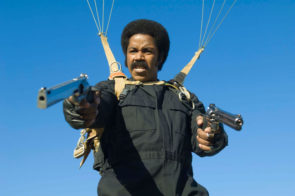 Michael Jai White håller fram två pistoler medan han använder en fallskärm mot den blå himlen i Black Dynamite
