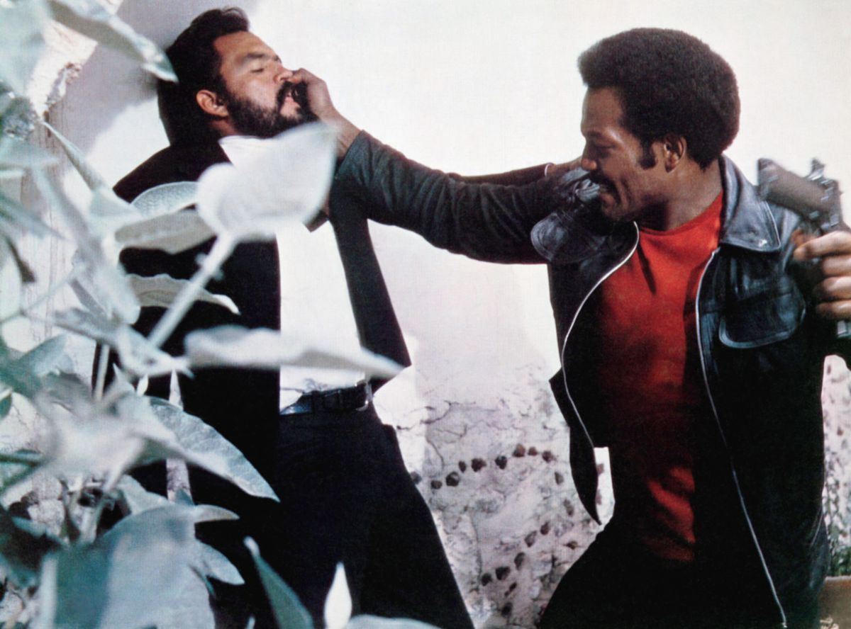 Jim Brown holds a man up against the wall and gets read to smack him with the butt of his gun in Slaughter.