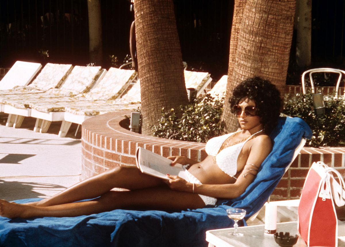 Pam Grier lounges by the pool in a white bathing suit in Coffy