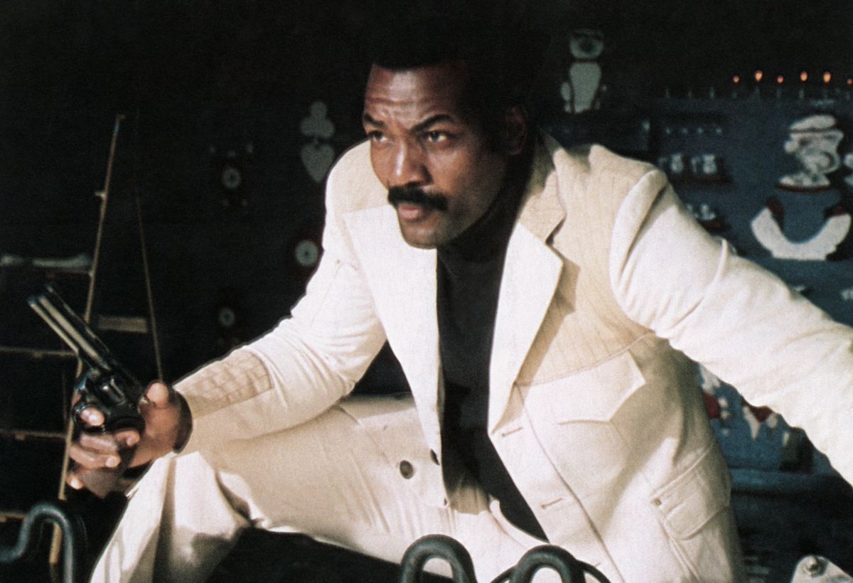 Jim Brown holds a revolver while wearing a slick white suit in Three the Hard Way