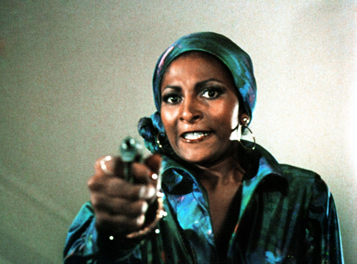 Pam Grier, wearing a head scarf, holds a pistol in Foxy Brown