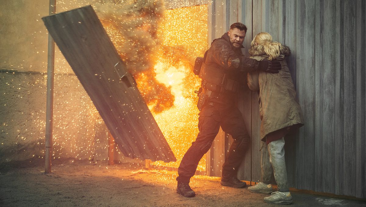 legosoldat Tyler Rake (Chris Hemsworth) och hans svägerska Ketevan (Tinatin Dalakishvili) skyddar mot en korrugerad metallvägg när en dörr i den väggen explosivt blåser upp i Extraction 2