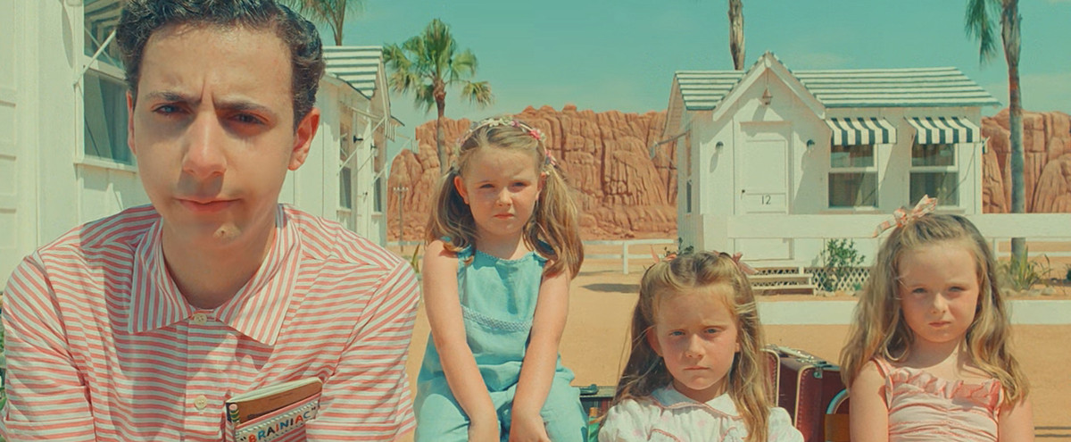 tonårspojken Woodrow Steenbeck (Jake Ryan) och hans trillingsyskon, tre unga flickor, sitter uppställda mot ett pastellvitt ökenmotell i Wes Andersons Asteroid City