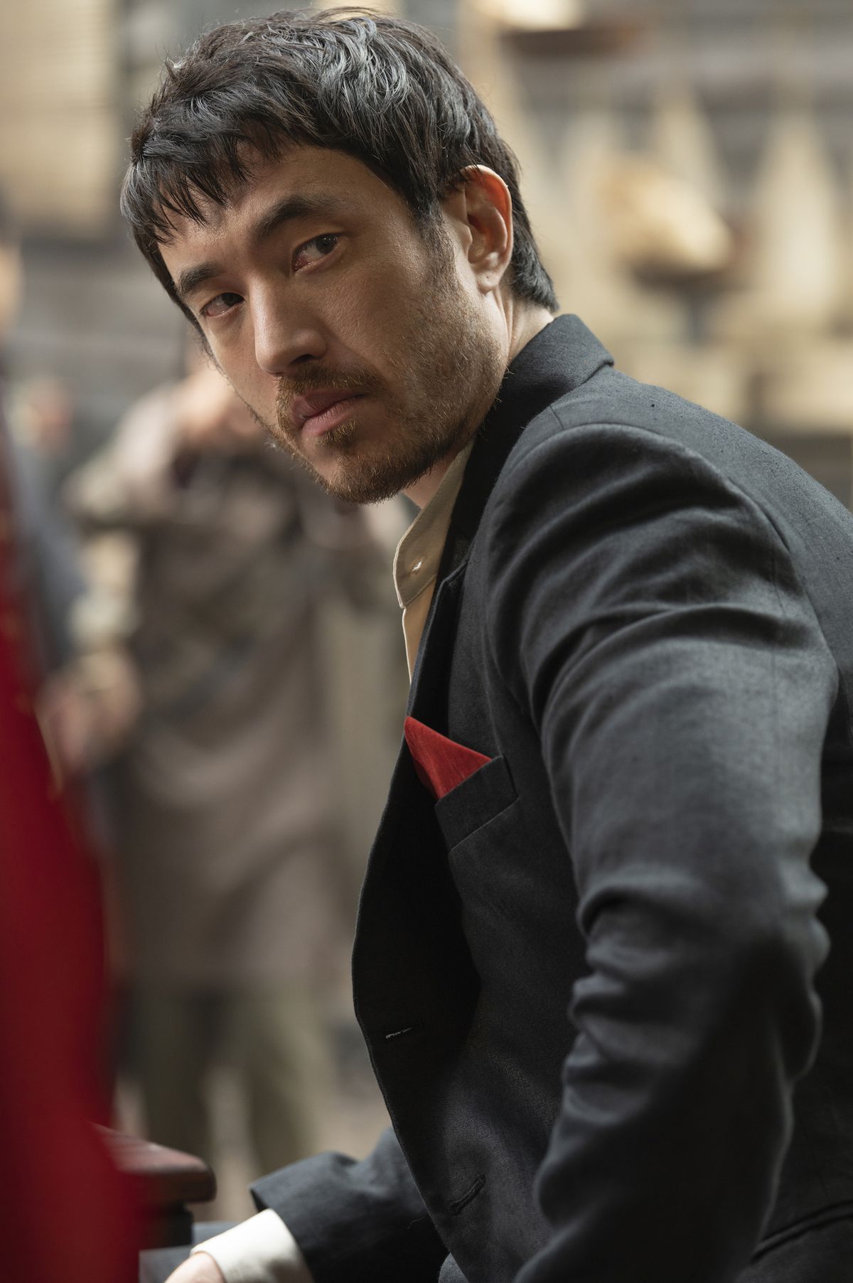 Andrew Koji looks over his shoulder, wearing a black suit and red handkerchief, in Warrior.